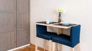 Een kleine eettafel met twee blauwe stoelen, een vaas met witte bloemen en borden en bestek op de tafel.