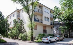 Um edifício residencial de vários andares com varandas, carros estacionados e árvores.