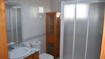 Une salle de bain avec un lavabo en marbre, un meuble en bois, des toilettes et une cabine de douche en verre.