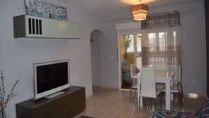 A modern living room with a flat-screen TV, a dining area with a table and chairs, and a hallway leading to another room. - Apartment with pool near the center and the beach (Puerto de Mazarrón)