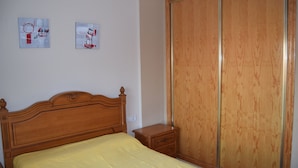 A bedroom with a wooden bed, a nightstand, a wardrobe, and two framed pictures on the wall. - Apartment with pool near the center and the beach (Puerto de Mazarrón)