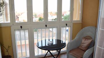 Une pièce avec une table en verre, une chaise en osier et une vue dégagée grâce à de grandes fenêtres.