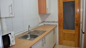 A kitchen with a sink, a microwave, and wooden cabinets. - Apartment with pool near the center and the beach (Puerto de Mazarrón)