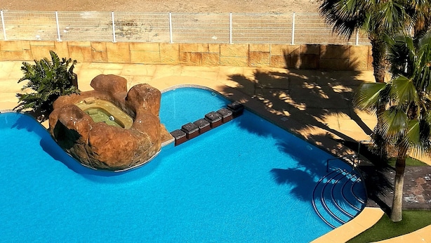 A swimming pool with a rock formation and palm trees. - Apartment with pool near the center and the beach (Puerto de Mazarrón)