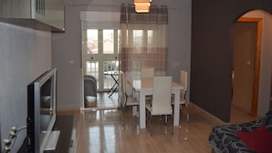 A modern living room with a flat-screen TV, a dining area with a table and chairs, and a cozy bed with a patterned blanket. - Apartment with pool near the center and the beach (Puerto de Mazarrón)