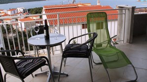 A balcony with a table and chairs, a view of a body of water, and red-tiled buildings in the background. - Modern apartment with amazing view (Trogir)