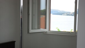 A bedroom with a single bed, a small bedside table, and a window overlooking a body of water and distant mountains. - Modern apartment with amazing view (Trogir)
