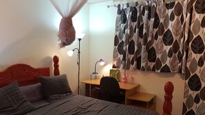 A bedroom with a bed, desk, and chair. There is a hanging mosquito net above the bed.