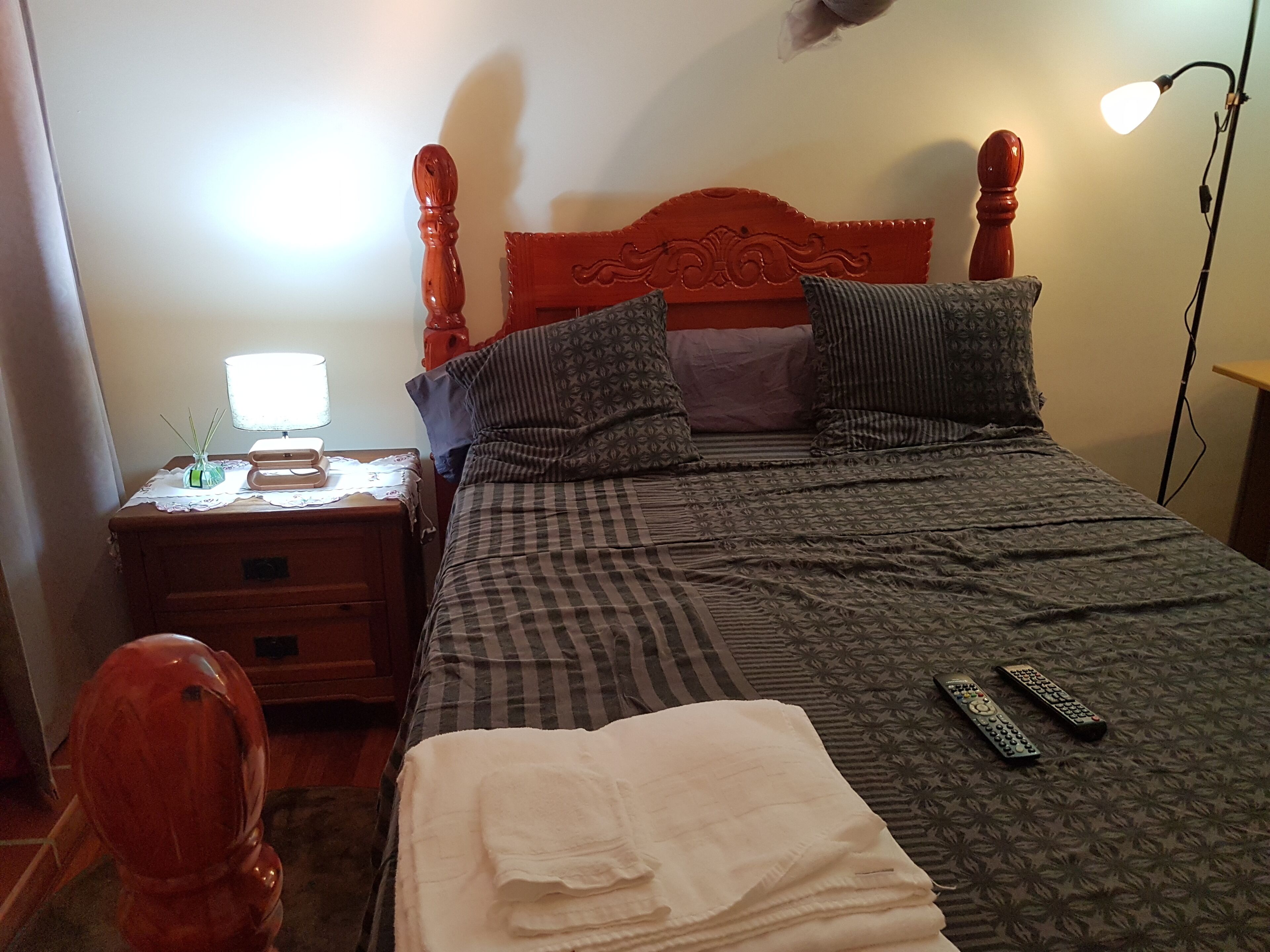 Ein ordentlich bezogenes Bett mit karierter Bettdecke, zwei Kissen und zwei Fernbedienungen.