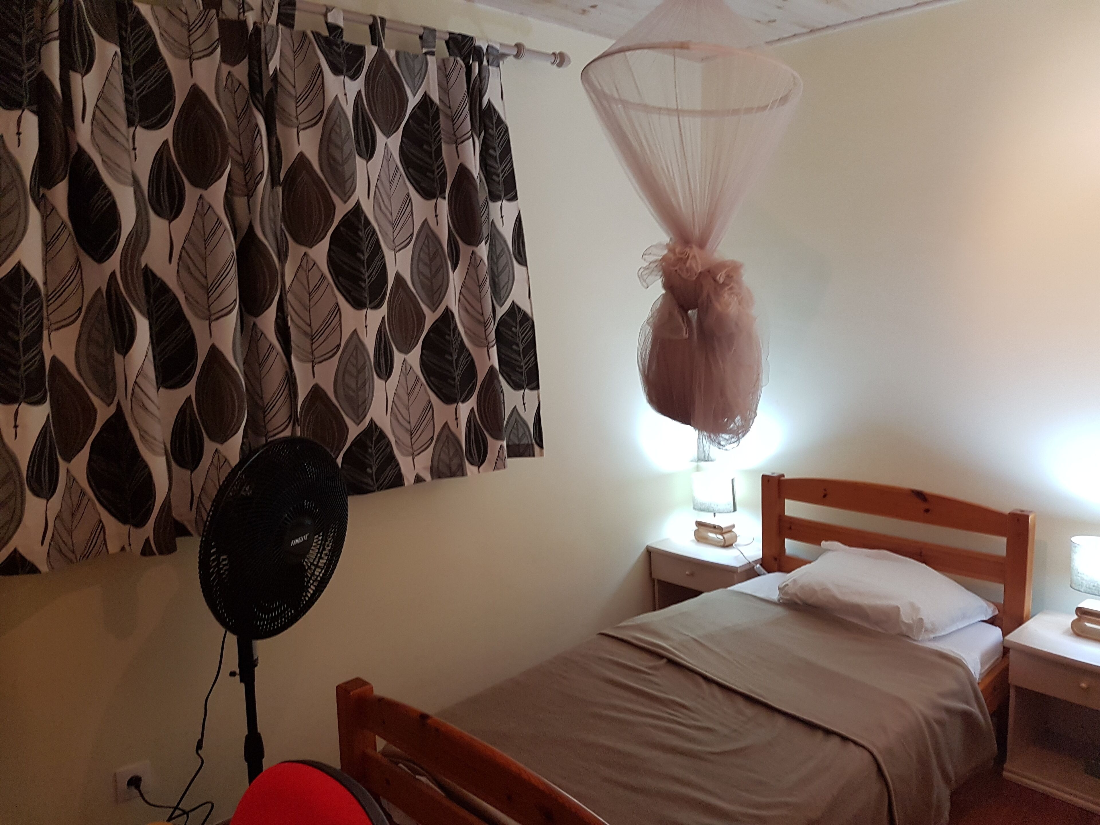 Ein Schlafzimmer mit einem Bett, einem Nachttisch, einem Wandventilator und einem Moskitonetz.