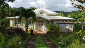 A two-story house with a tiled roof, a front porch, and a garden with various plants and a pathway leading to the entrance.