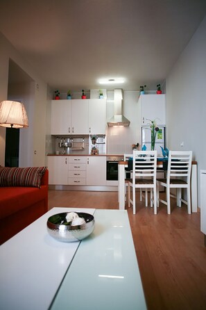 Um espaço compacto com cozinha compacta, área de refeições com cadeiras brancas e sofá vermelho.