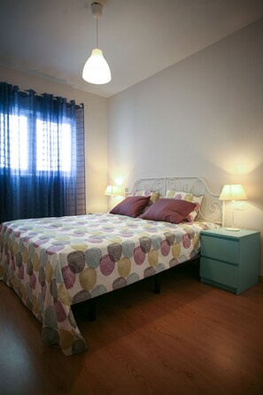 Quarto com cama, duas mesas de cabeceira com luminárias, janela com cortinas e uma luminária no teto.