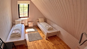 Um quarto de sótão pequeno e acolhedor com duas camas de solteiro, uma janela e chão de madeira.