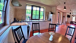 Uma cozinha espaçosa com uma janela grande, uma área de jantar com mesa redonda, e uma sala de estar com sofá e televisão.