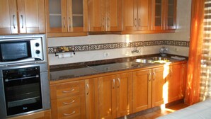 Una cocina con armarios de madera, microondas, horno, lavaplatos y un salpicadero decorativo de azulejos.