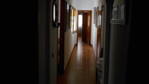 Un pasillo estrecho con suelo de baldosas, puertas de madera y cuadros en las paredes.