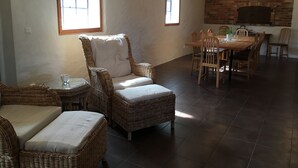 Un espace repas agrémenté d’un mur en briques, de poutres en bois au plafond et d’une cheminée en briques. On y trouve des chaises en osier et une table à manger avec des chaises.