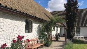 Un bâtiment blanc avec un toit en tuiles, un banc en bois et un jardin fleuri.