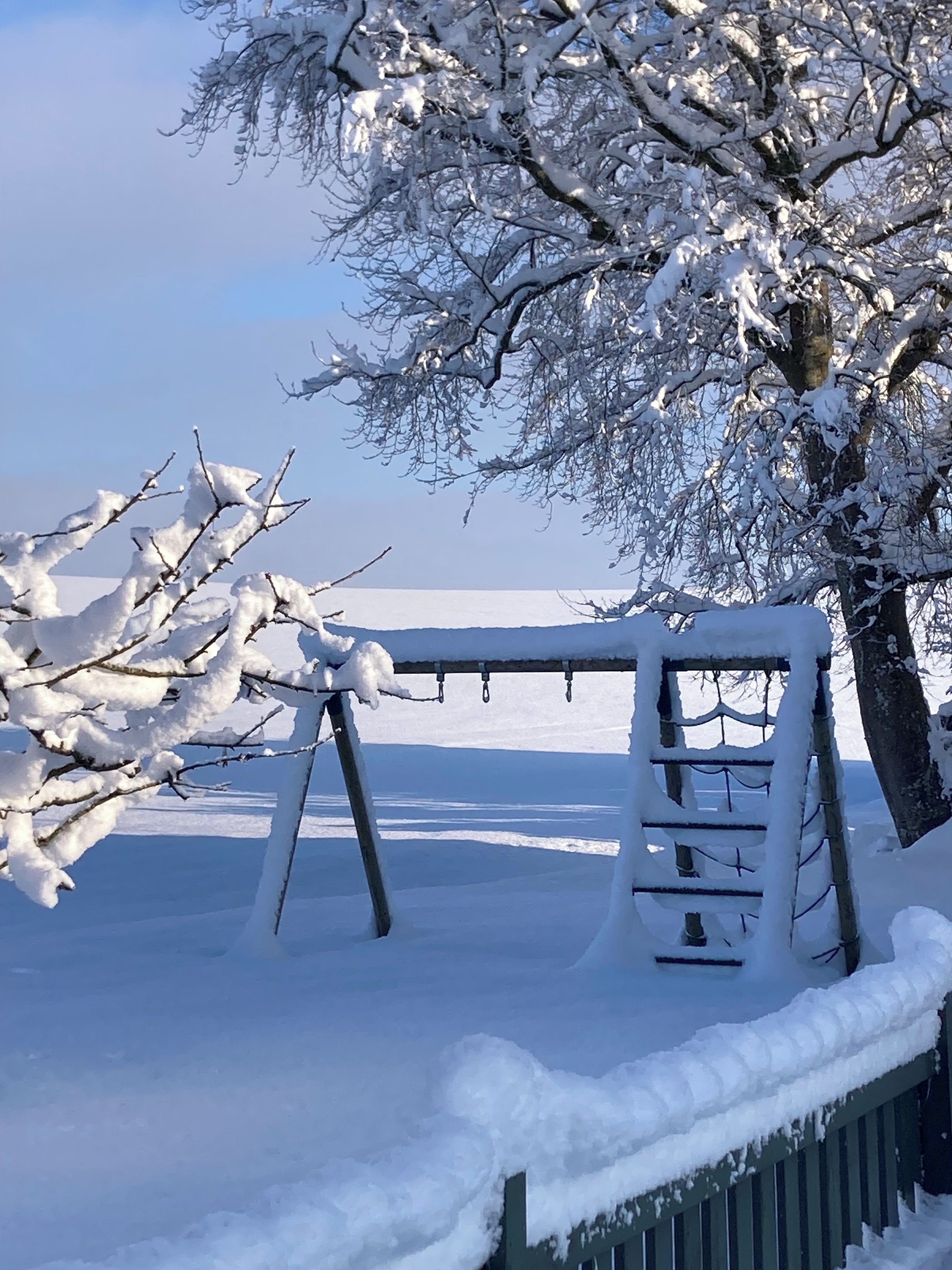 A snow-covered swing set in a park with a clear sky.