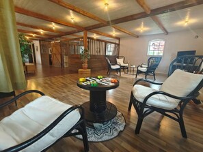A spacious room with a high ceiling, wooden beams, and a round table with a board game. There are several chairs around the table and a potted plant in the corner. - Unique living in converted horse stable (Ystad V)