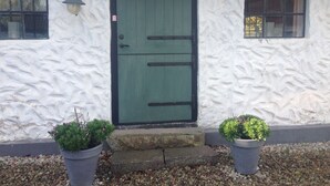 Un bâtiment avec une porte verte, deux fenêtres et deux plantes en pot.