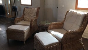 Une pièce comprenant deux fauteuils en osier, une petite table, une plante en pot et une porte.