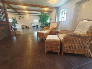 A spacious room with dark wooden flooring, a large wicker sofa set, and a dining area with chairs and a table. - Unique living in converted horse stable (Ystad V)