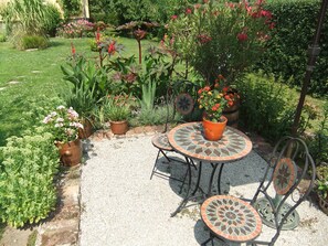 Une terrasse de jardin avec une table et des chaises décorées de motifs en mosaïque, entourée de différentes plantes et fleurs en pot.