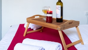 Ein Bett mit roter Decke, ein Holztablett mit einer Weinflasche, einem Weinglas und einer Kerze.