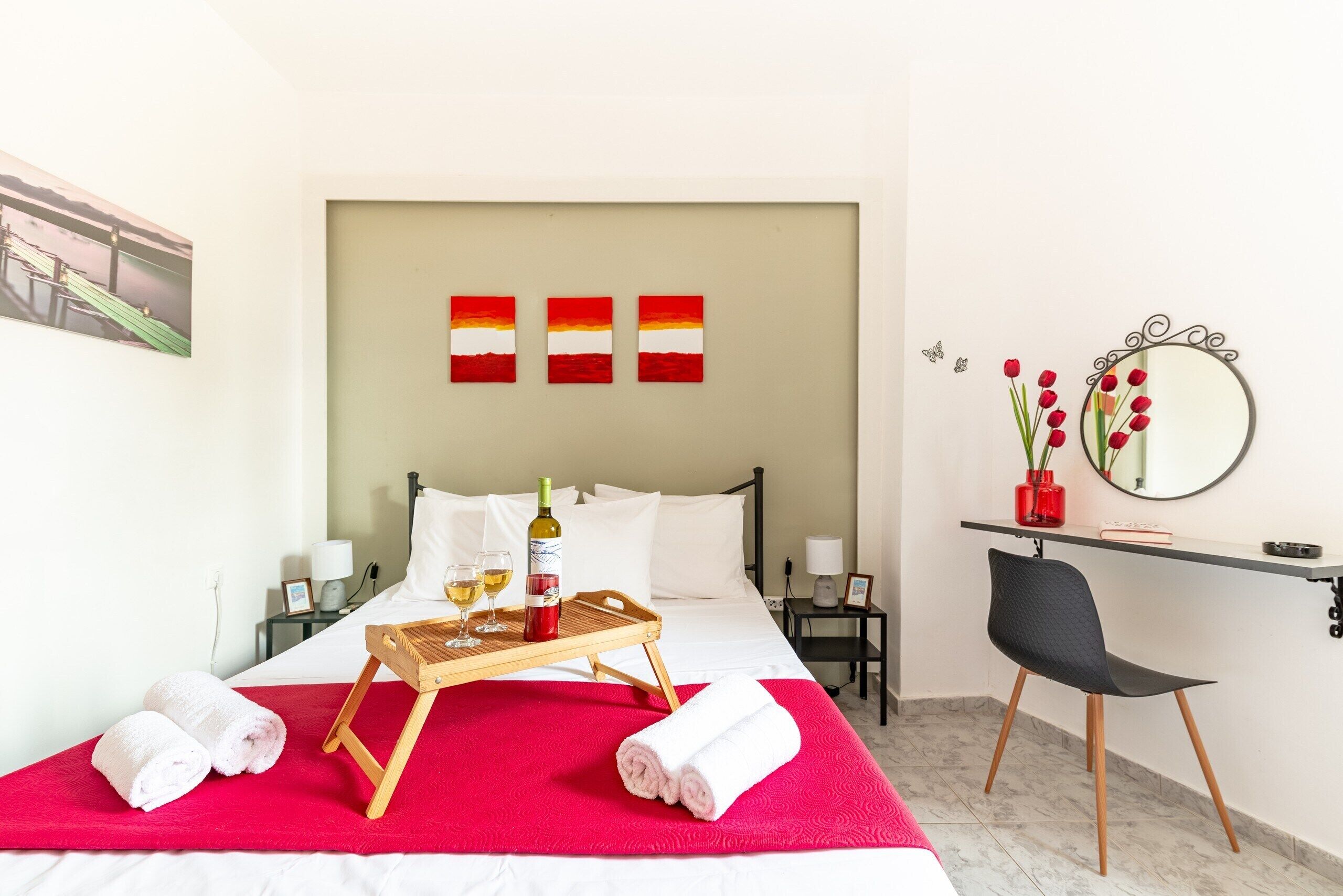 Ein Hotelzimmer mit einem Bett, einem Schreibtisch, einem Stuhl, einem Tablett mit Handtüchern und einer Flasche sowie einem Spiegel an der Wand.