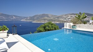 A clear blue swimming pool with a view of the sea and mountains in the background.