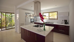 A modern kitchen with a central island, white cabinets, and a large window providing a view of greenery.