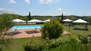 Ein Poolbereich mit Sonnenschirmen und Liegestühlen, umgeben von Grünflächen und Hügeln im Hintergrund.