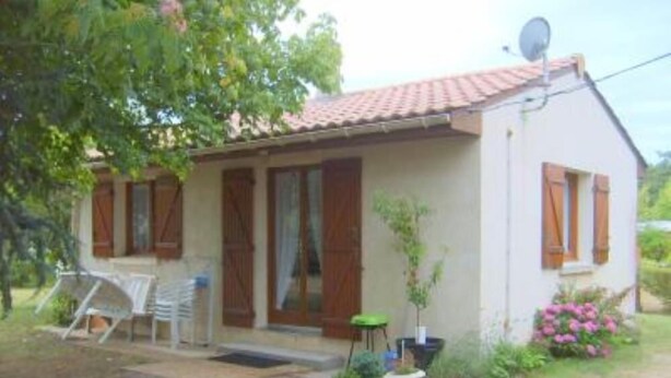 Ein kleines Haus mit Ziegeldach, Holzklappläden und einer Satellitenschüssel.