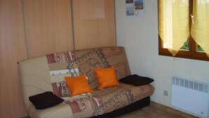 Ein kleines, möbliertes Zimmer mit einer Couch, zwei Kissen, einem Fenster mit Vorhängen und einer Heizung.