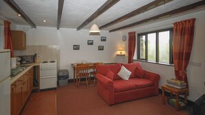 Een compacte woonruimte met een kitchenette, een rode bank, een eettafel en een televisie.