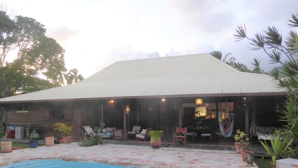 Una casa con piscina, terraza techada y zona de estar exterior con sillas y mesas.
