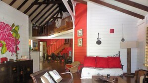 Un salón espacioso con techo alto, una escalera, un comedor y un sofá con cojines rojos.