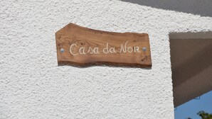 Ein hölzernes Schild mit der Aufschrift 'Casa da Nor' an einer strukturierten weißen Wand befestigt.