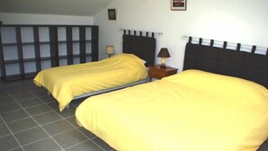 Een kamer met twee bedden, elk met een hoofdeinde, een nachtkastje met een lamp en een betegelde vloer.