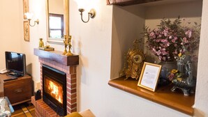 Ein Kamin mit Fernseher auf einer Holzkommode, darüber ein Spiegel und eine Ablage mit einer Uhr und Blumen.