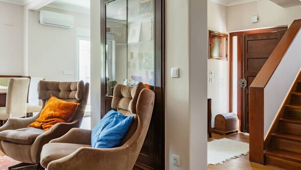 Ein Wohnzimmer mit zwei Sesseln, einer Glastruhe und einer Holztreppe.