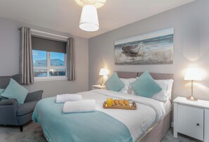 Ett hotellrum med en säng, en stol, ett nattduksbord, en lampa och en tavla med ett motiv av en båt på väggen.