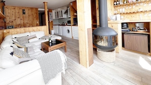 Ett kompakt vardagsrum med en soffa, ett soffbord, en öppen spis, en köksdel och ett vinställ.