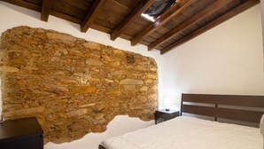 Ein Schlafzimmer mit Steinwand, Holzbalkendecke, einem Bett mit weißer Bettwäsche und einem Nachttisch.