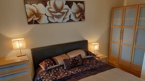 A bedroom with a bed, two bedside tables, a wardrobe, and a floral artwork on the wall. - Waterfront apartment in the Heart of St Neots (St Neots, Cambs)