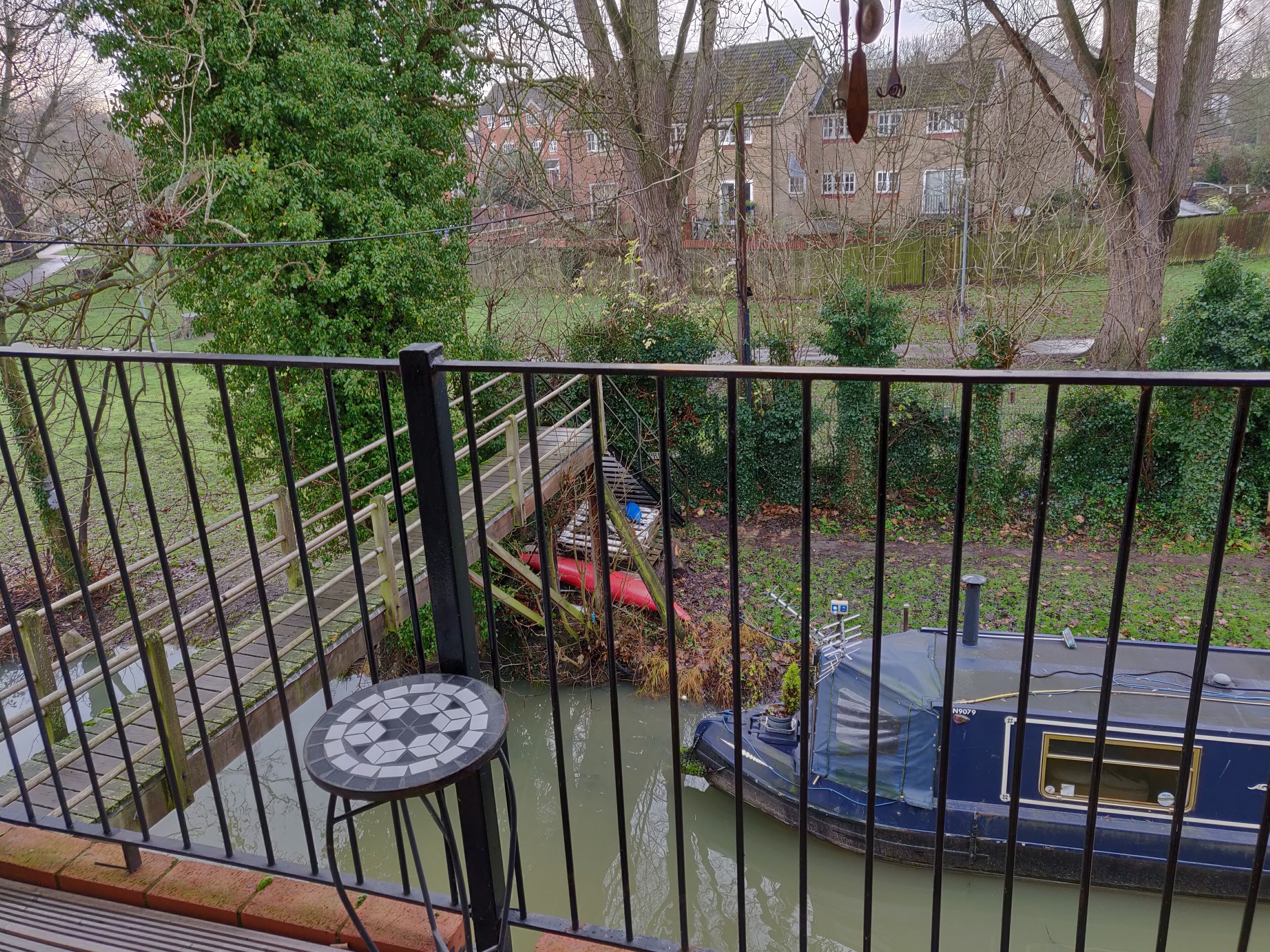 A view from a balcony overlooking a canal with a boat, a wooden bridge, and greenery.