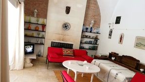 Ein Wohnzimmer mit einem roten Sofa, einem weißen Tisch und einem Fernseher. Es gibt Regale mit Dekoration und eine Ziegelwand.