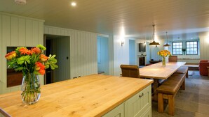 A spacious kitchen with wooden countertops, a dining table, and benches. There is a vase with flowers on the countertop.